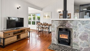 Una sala de estar moderna con chimenea de piedra, piso de madera, televisor y comedor con sillas.