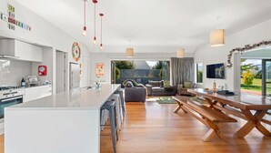 Eine moderne Küche mit Kochinsel, ein Essbereich mit Holztisch und Bänken sowie ein Wohnzimmer mit Sofa und Fernseher.
