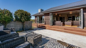 Ein modernes Haus mit überdachter Terrasse, Sitzgelegenheit im Freien und Blick auf den Garten.