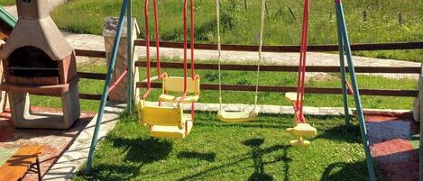 Un parque infantil con columpios y un horno de piedra.