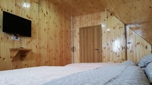 A wooden-paneled room with a bed, a TV mounted on the wall, and a door. - Rocky Mountain Triple Room (Prisoje)