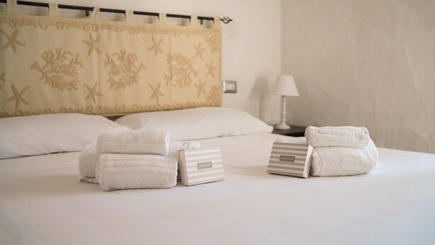 A neatly made bed with folded towels and a bedside table with a lamp. - MareSole La Cinta - Two Bedroom Apartment, Sleeps 6 (San Teodoro)