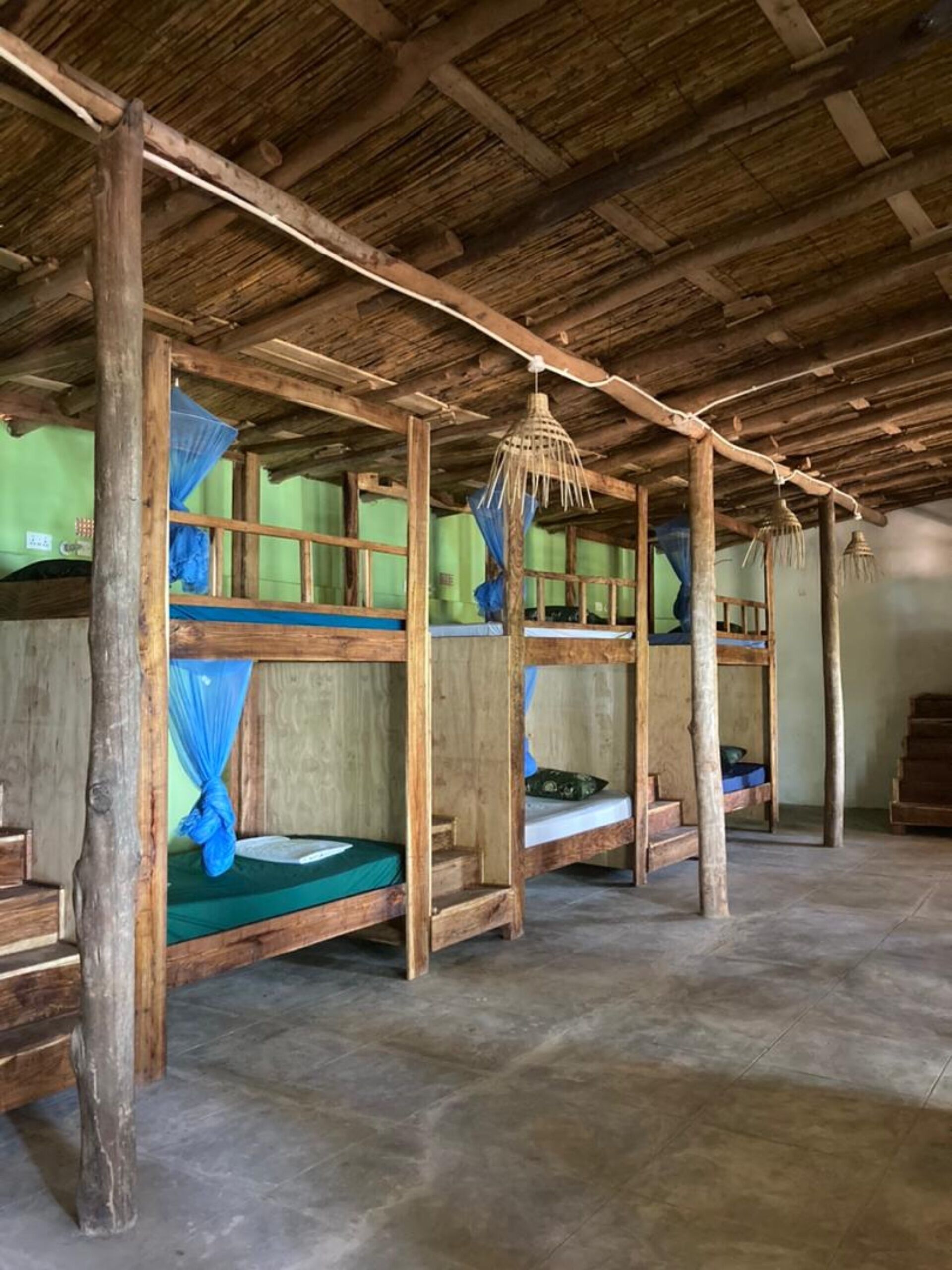 A rustic wooden room with bunk beds, a woven basket hanging from the ceiling, and a green wall.