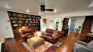A spacious living room with a leather sofa set, a coffee table, and a bookshelf filled with books and decorative items. - Old Town Charmer Large all new renovation, walk to USM, Zoo and new Water Park! (Hattiesburg)
