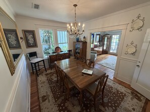 A dining area with a wooden table, chairs, a chandelier, and a view of the outdoors.