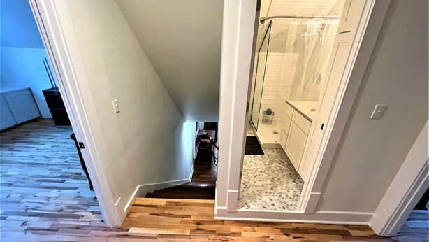 A hallway with a wooden herringbone floor leading to a bathroom with a glass shower enclosure and white tiles. - Old Town Charmer Large all new renovation, walk to USM, Zoo and new Water Park! (Hattiesburg)