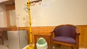 A room with a wooden chair, a small table, a refrigerator, and a yellow pole with hooks. - WAYU HOUSE (Dawu)