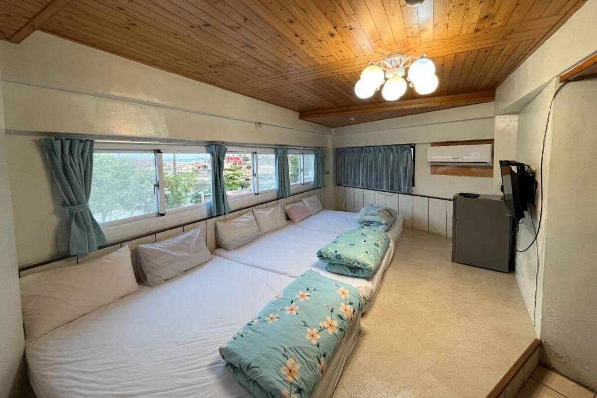 Una habitación con techo de madera, una cama con colcha estampada, un escritorio con computadora y una ventana con cortinas.