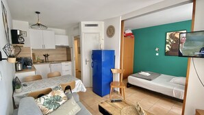 Un espace de vie compact comprenant un coin cuisine, un coin repas, un canapé, une télévision et un lit.