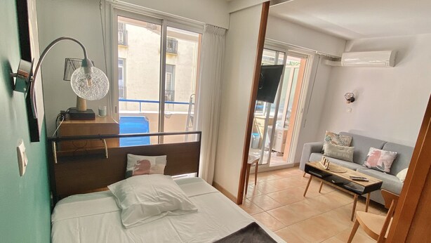 Une chambre à coucher comprenant un lit, une table de chevet, une lampe, une fenêtre, un balcon et un canapé.