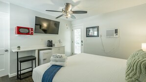 A hotel room with a bed, a desk with a microwave, a television, a ceiling fan, and an air conditioning unit.