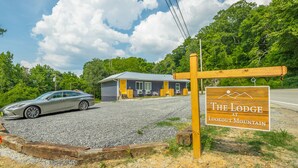 A lodge sign with a mountain view, a gravel driveway, and a parked car.