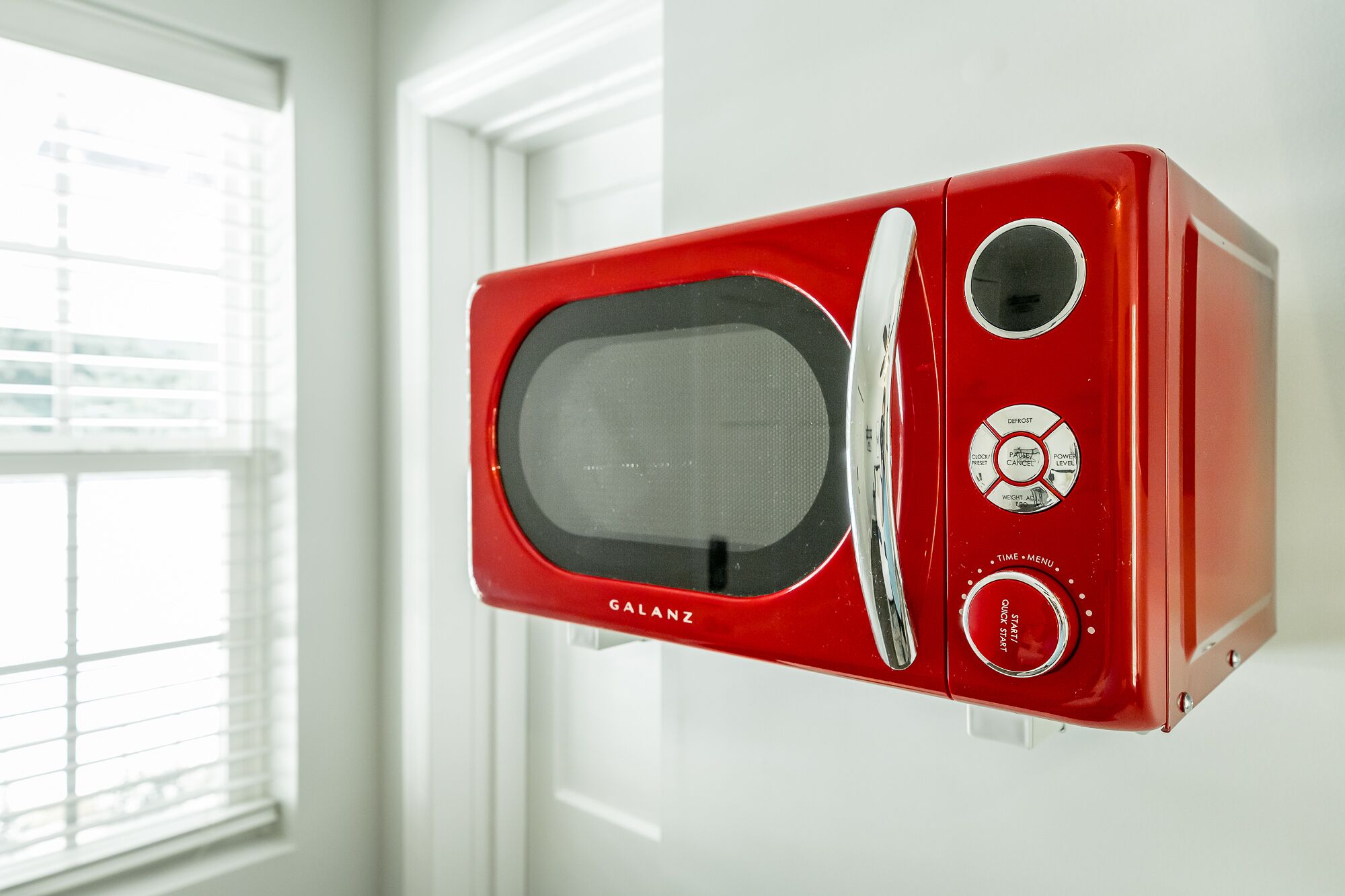 A red microwave oven with a handle, brand name 'GALANZ', and control buttons including 'DEFROST', 'CLOCK/RESET', 'POWER LEVEL', and 'WEIGHT ADJUST'.