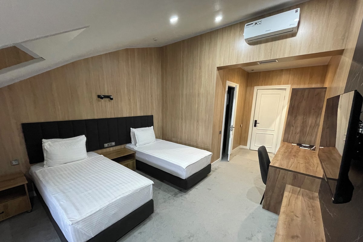 A hotel room with two beds, a wooden desk, a TV, and an air conditioning unit.