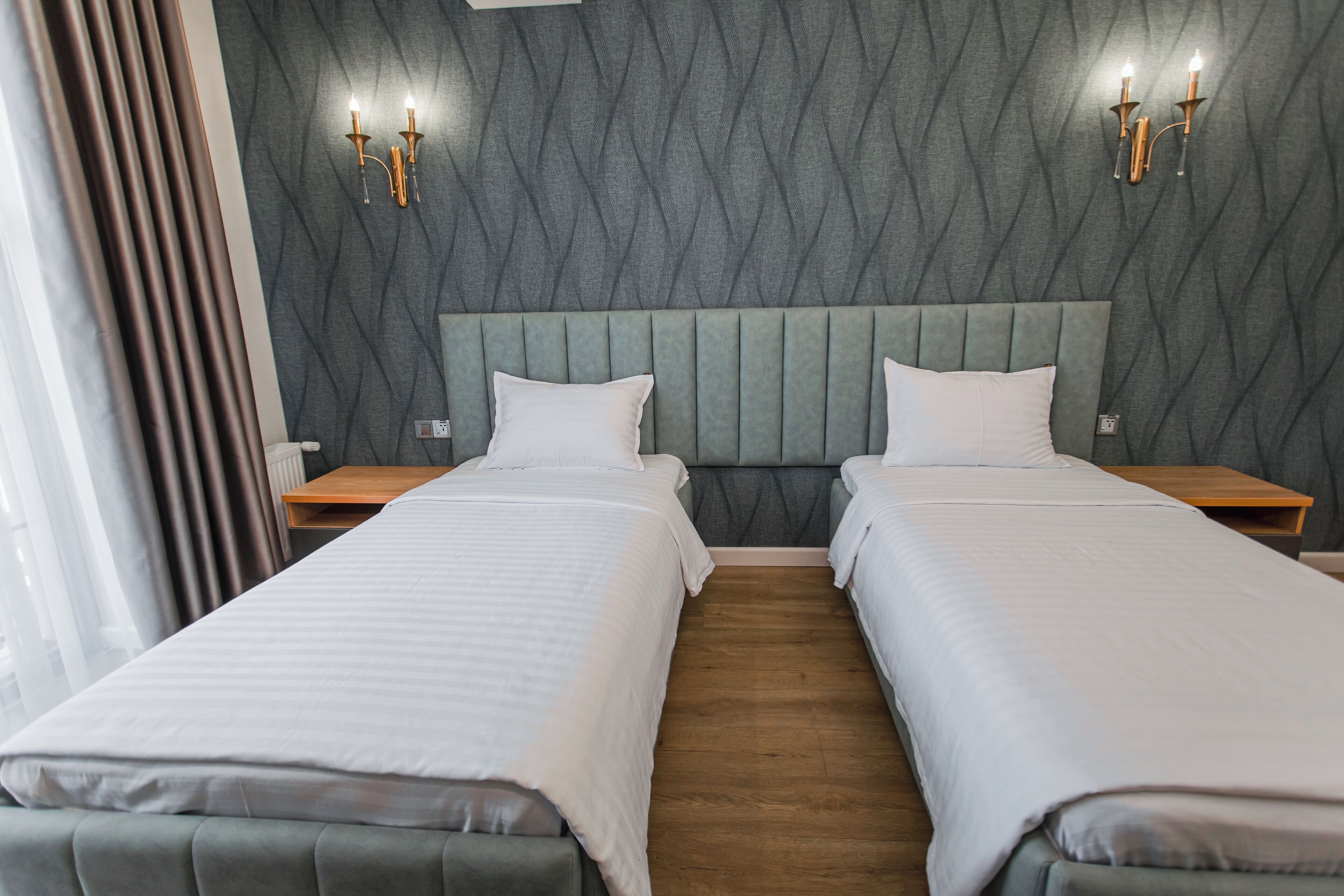 Ein Hotelzimmer mit zwei Betten, einer grauen Wand mit Struktur und einem Holzboden.