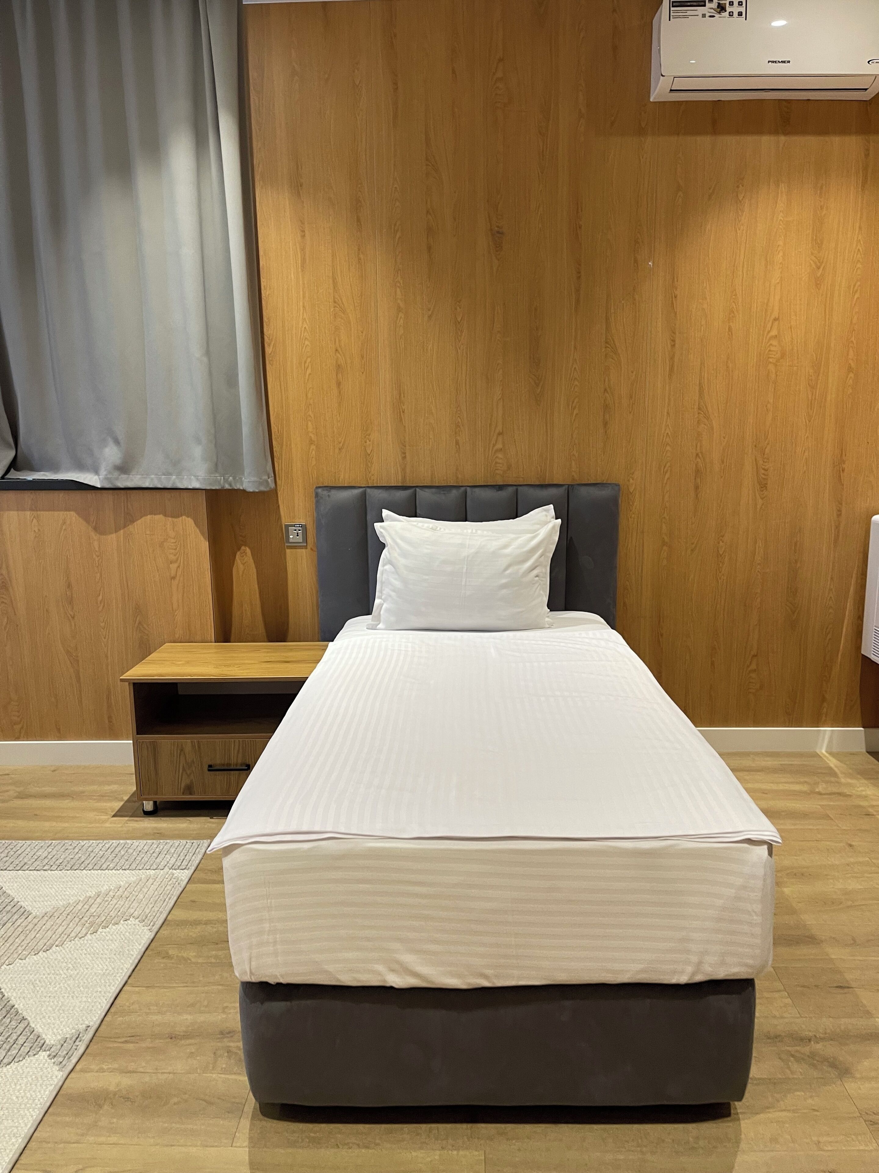 A neatly made bed with a grey headboard and white bedding in a room with wooden panel walls.