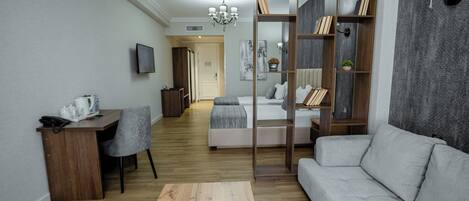 Een moderne woonkamer met een bank, een salontafel, een bureau en een boekenkast. In de achtergrond staat een bed met uitzicht op de gang.