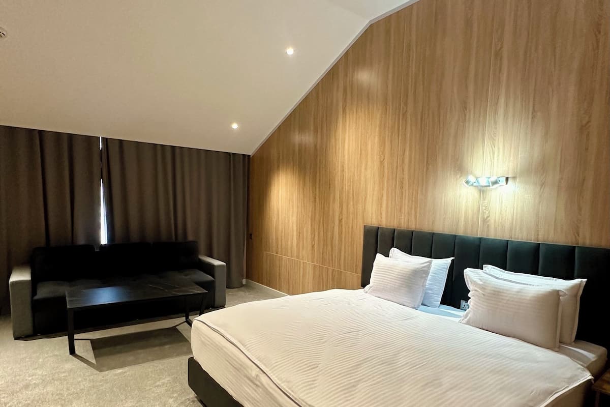 A modern bedroom with a large bed, a dark sofa, and a wooden accent wall.