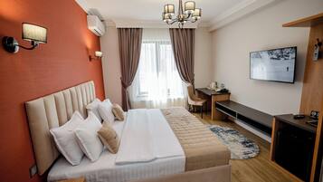 A hotel room with a large bed, a desk, a television, and a chair.