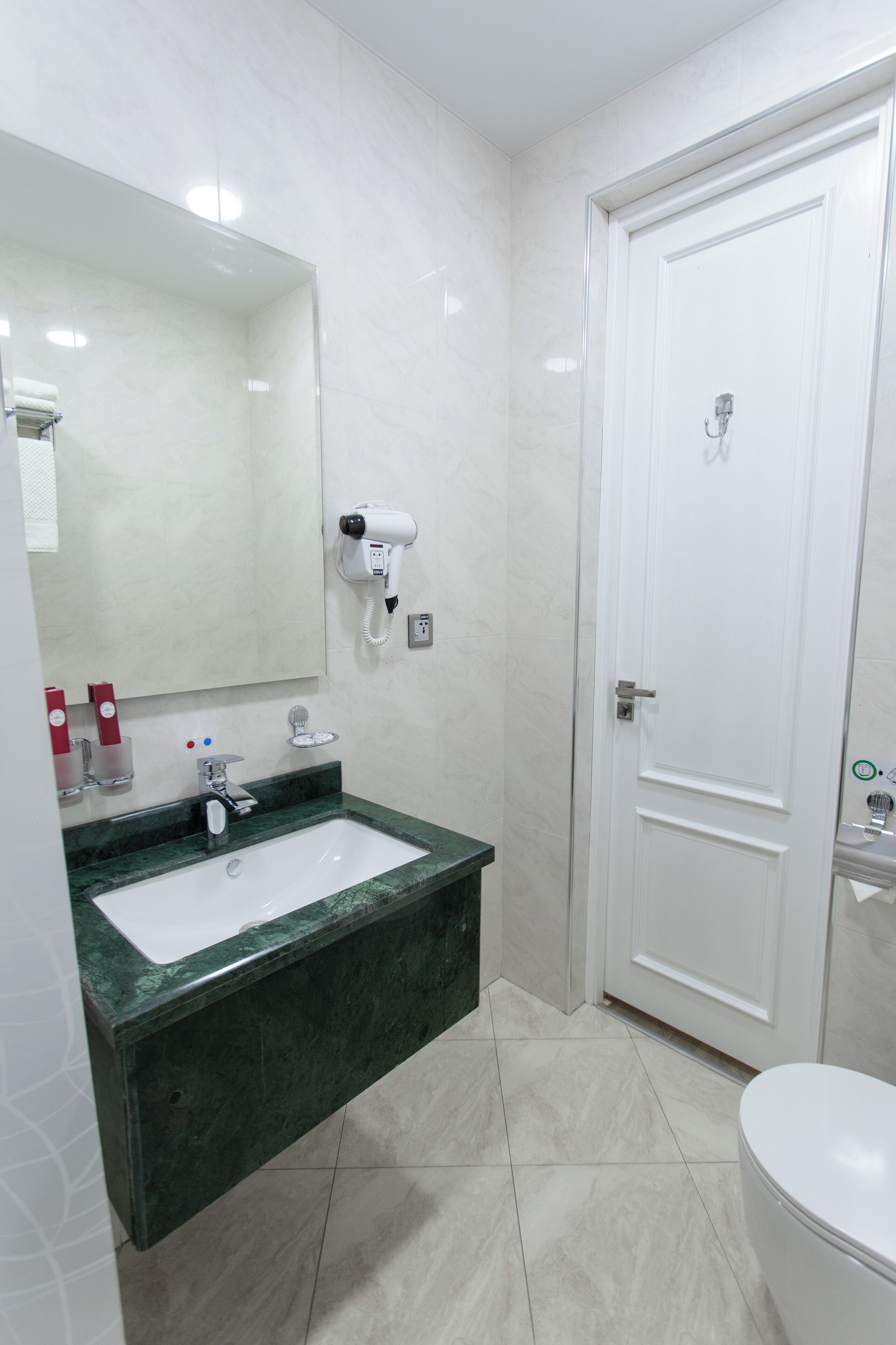 A bathroom with a white sink, green marble countertop, and a white toilet.
