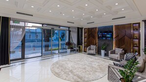 A spacious lobby with a large round rug, seating area with sofas, and a TV screen on the wall. - WELLFORT HOTEL (Samarkand)
