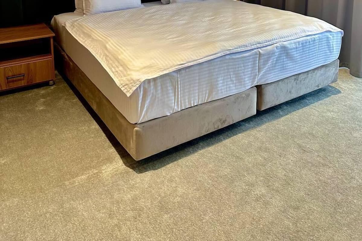 A hotel room with a large bed, wooden panel wall, and a dark headboard.