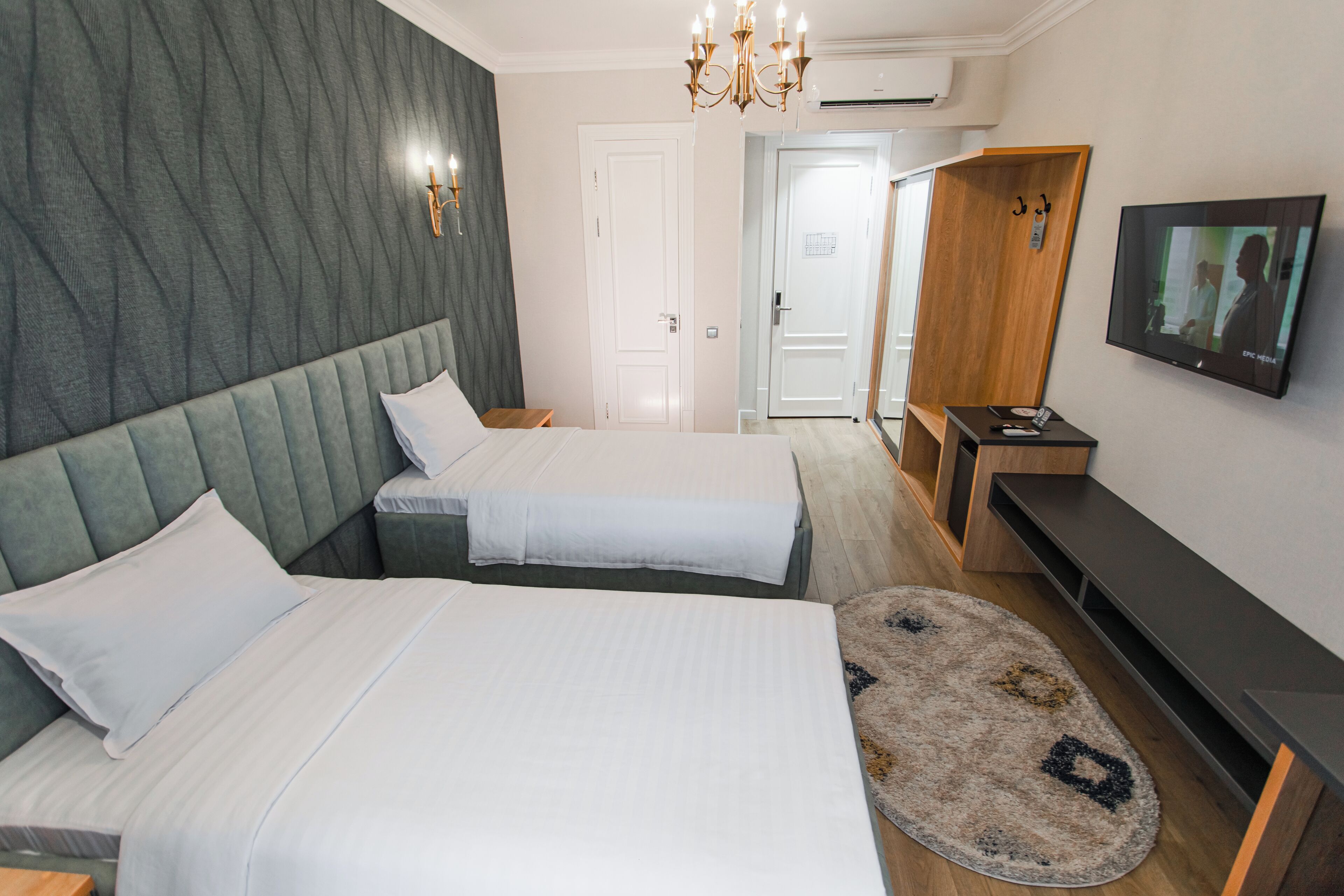 A hotel room with two beds, a TV, a wooden wardrobe, and a round rug.