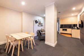 Un apartamento moderno con comedor, sofá, sillón estampado, cocina con muebles de madera y encimera negra.