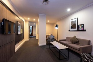 Ein modernes Wohnzimmer mit einer Couch, einem Couchtisch, einem an der Wand montierten Fernseher und einem Flur, der zu einem Essbereich führt.