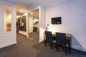 Habitación de hotel con escritorio, dos sillas, televisor de pantalla plana y puerta de vidrio que da a otra habitación.