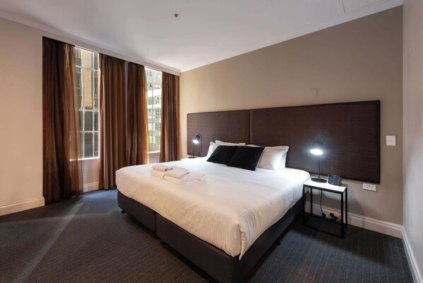 A hotel room with a large bed, a nightstand, a lamp, and a view of the outside through the window.