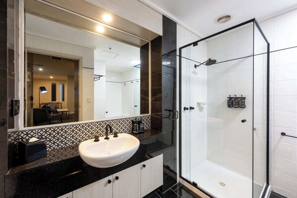 A modern bathroom with a large mirror, a white sink, a glass-enclosed shower, and a patterned tile backsplash.