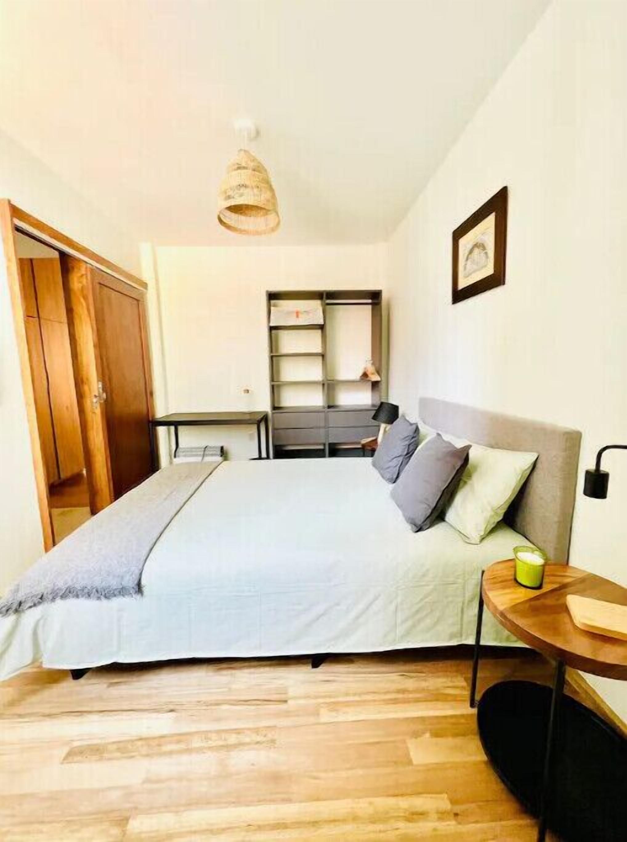 Een slaapkamer met een bed, nachtkastje, lamp, plank en kast.