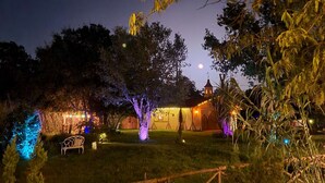 A rustic outdoor setting with a wooden structure, possibly a cabin, surrounded by trees and illuminated by string lights. - Schneewittchen Cottage (#3) (Fredericksburg)