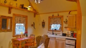 A cozy kitchen with wooden cabinets, a dining table with chairs, and a patterned armchair. - Schneewittchen Cottage (#3) (Fredericksburg)