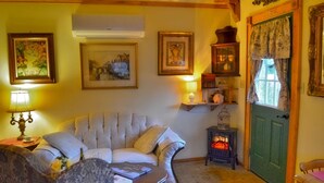 A cozy living room with a plush sofa, a table with books, a decorative lamp, and a vintage stove. - Schneewittchen Cottage (#3) (Fredericksburg)