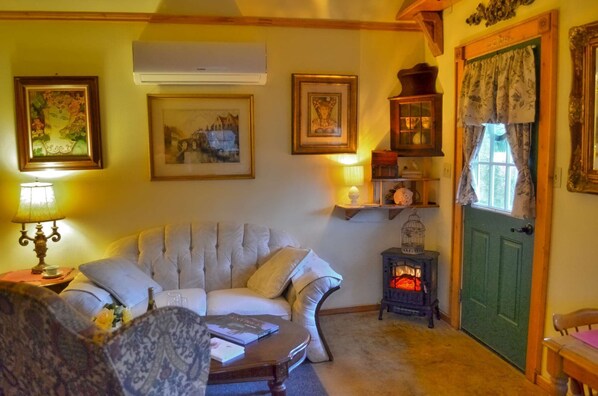 A cozy living room with a plush sofa, a table with books, a decorative lamp, and a vintage stove. - Schneewittchen Cottage (#3) (Fredericksburg)