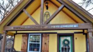 A building with a yellow facade, a green door, and a sign above the entrance. - Schneewittchen Cottage (#3) (Fredericksburg)