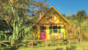 A small, colorful house with a sloped roof, surrounded by lush greenery and a wooden fence. - Aschenputtel Cottage (#4) (Fredericksburg)