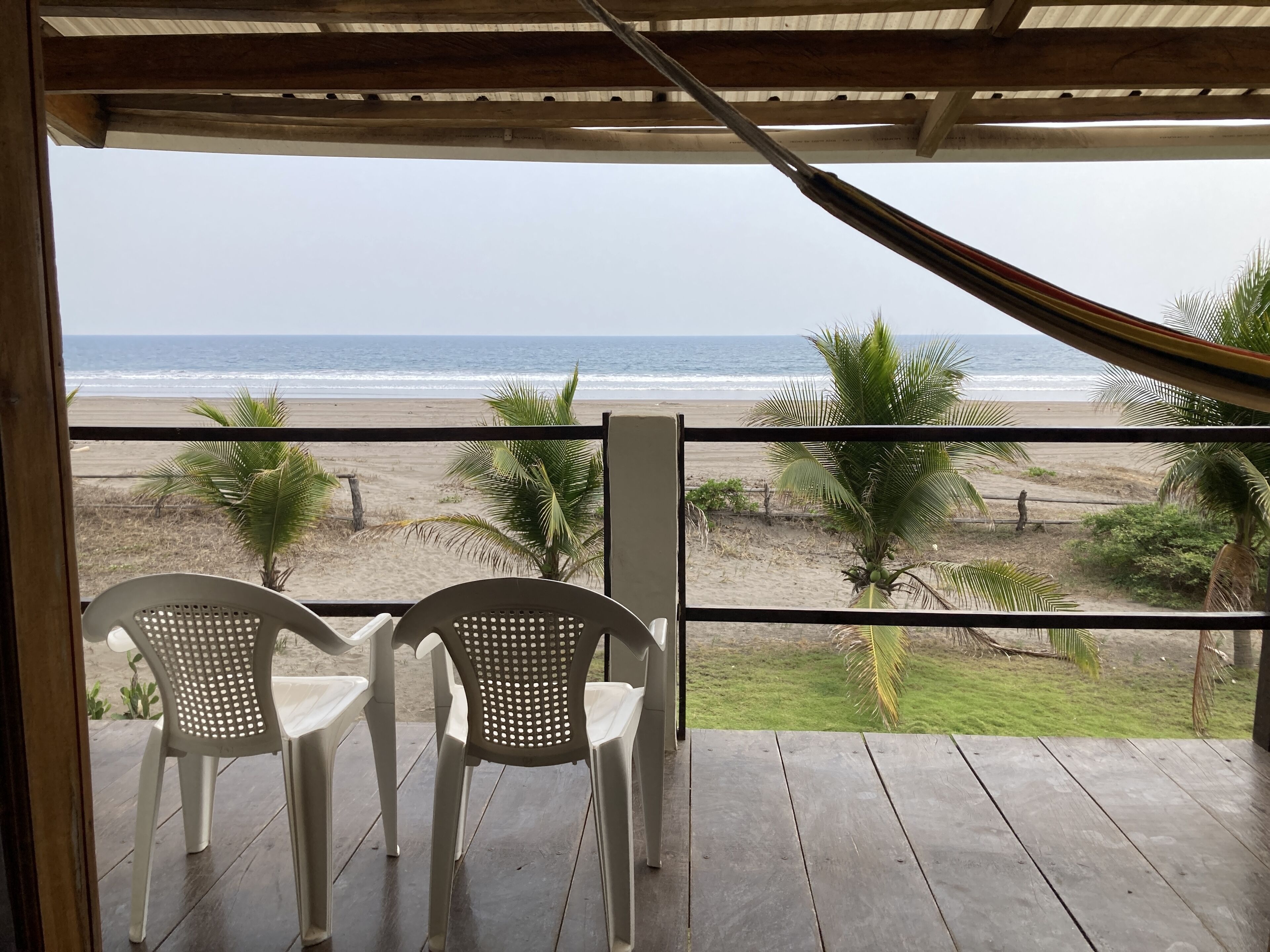 Una terraza de madera con dos sillas de plástico blanco que dan a la playa.