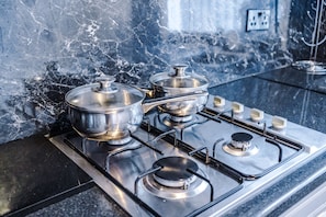 Cozinha com fogão a gás, panelas e painel de fundo em mármore.