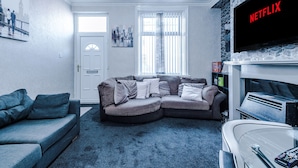 A living room with a sectional sofa, a television mounted on the wall, and a door leading to another room.