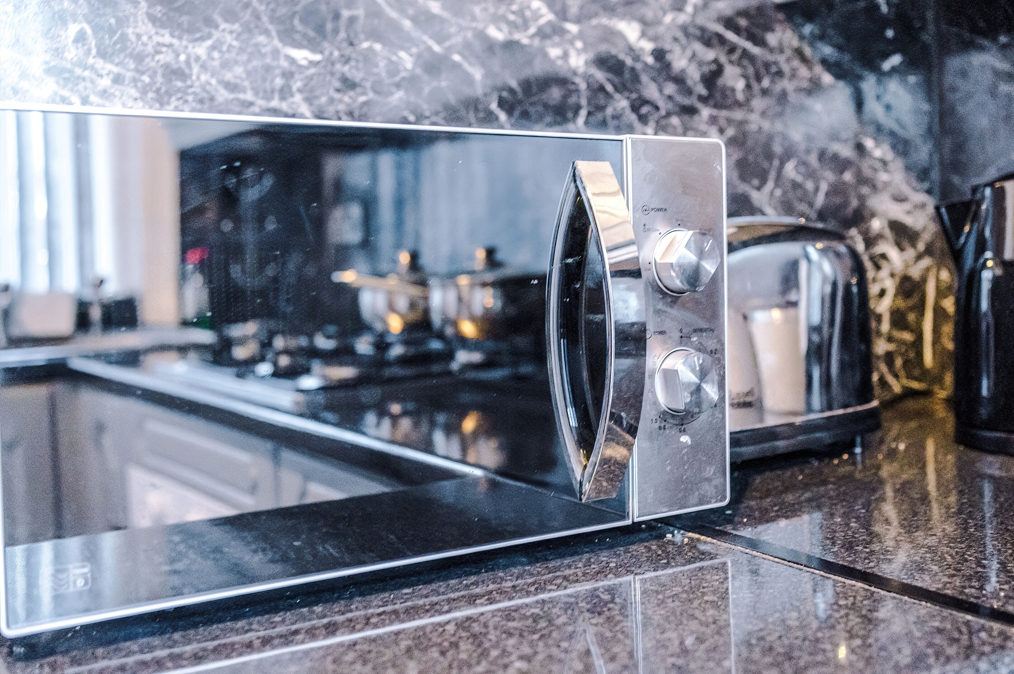 A kitchen with a stainless steel microwave, a toaster, and a marble backsplash.
