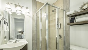 Ein modernes Badezimmer mit einer Duschkabine aus Glas, einem weißen Waschbecken und einem Waschtisch mit dunklen Schränken.