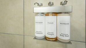 Ein Badezimmerschrank mit drei Flaschen Pflegeprodukten: Nourish Replenishing Conditioner, Clean Invigorating Shampoo und Refresh Moisturizing Body Wash.
