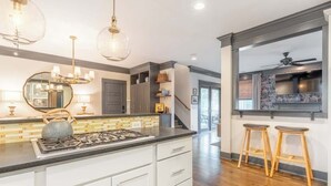A modern kitchen with white cabinets, a gas stove, and a large mirror. There are wooden stools and a ceiling fan visible. - The Mont Rose - Walkable to 12 South (Nashville)
