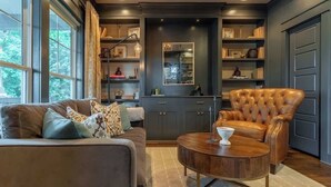 A modern living room with a leather armchair, a wooden coffee table, and a sofa with patterned cushions. - The Mont Rose - Walkable to 12 South (Nashville)
