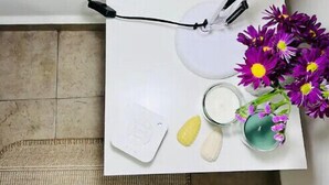 Ein Badezimmer mit Waschbecken in Weiß, einem weißen Handtuch, einer kleinen weißen Seifenschale, einem Glas Wasser und einem Glas Milch, sowie einer Vase mit lila Blumen.