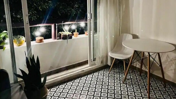 Ein Balkon mit weißem Stuhl und Tisch, Topfpflanzen und einem gemusterten Boden.