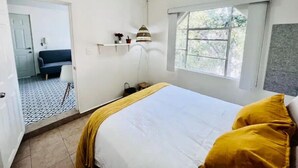 Ein Schlafzimmer mit Bett, Fenster, Tür und einem kleinen Tisch mit Lampe.